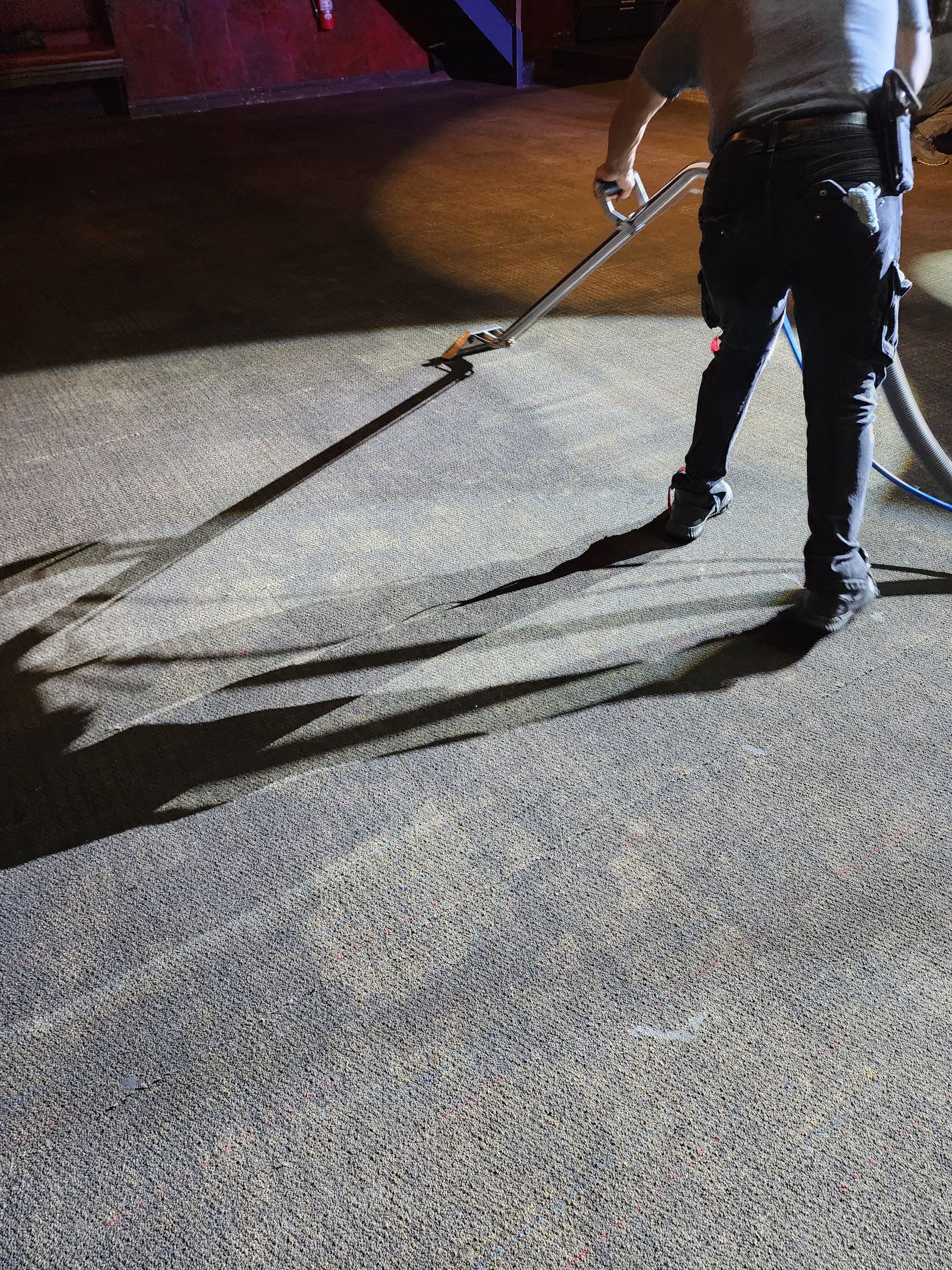 A person using a floor cleaning machine on a textured concrete surface under artificial lighting.