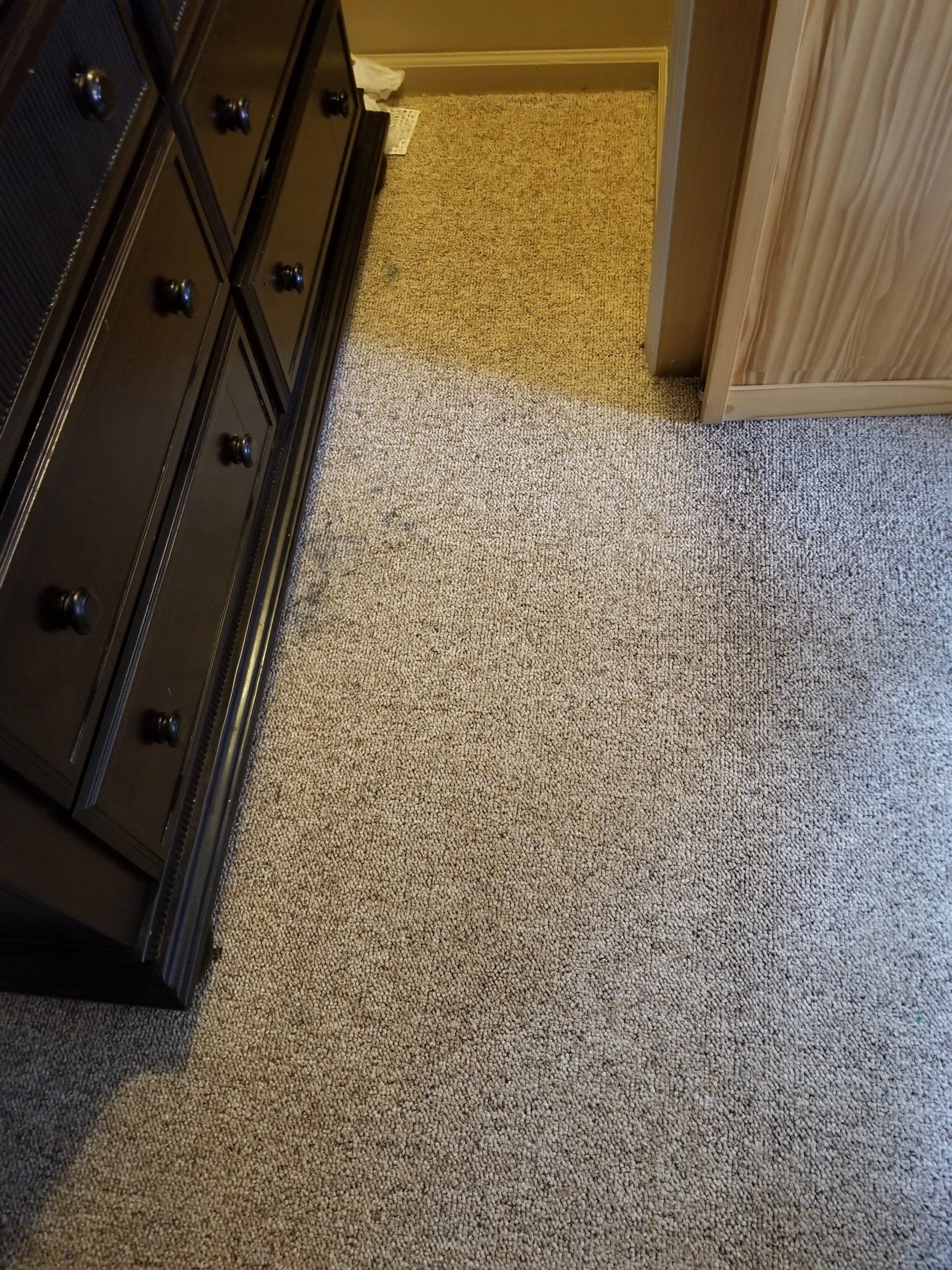 A dark brown wooden dresser sits on gray and white patterned carpet next to a light wood door frame.