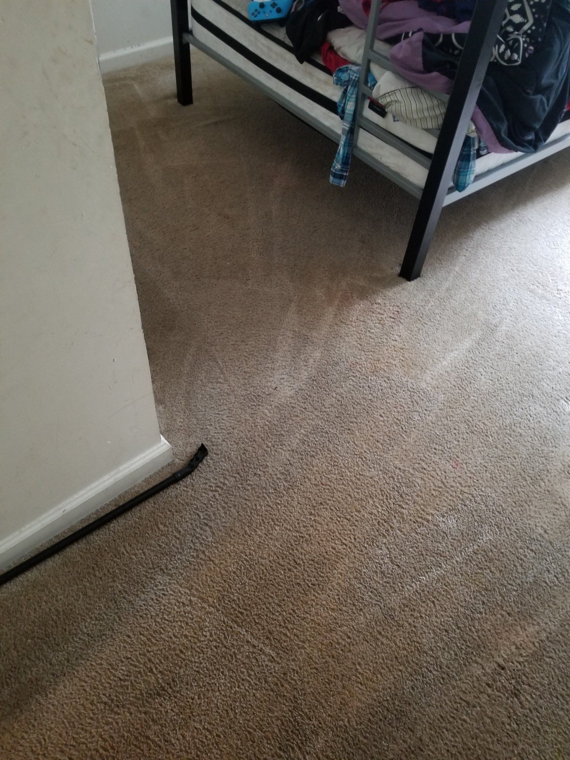 A brown carpeted floor with a black bed frame corner and a dark wire extending from a wall corner.