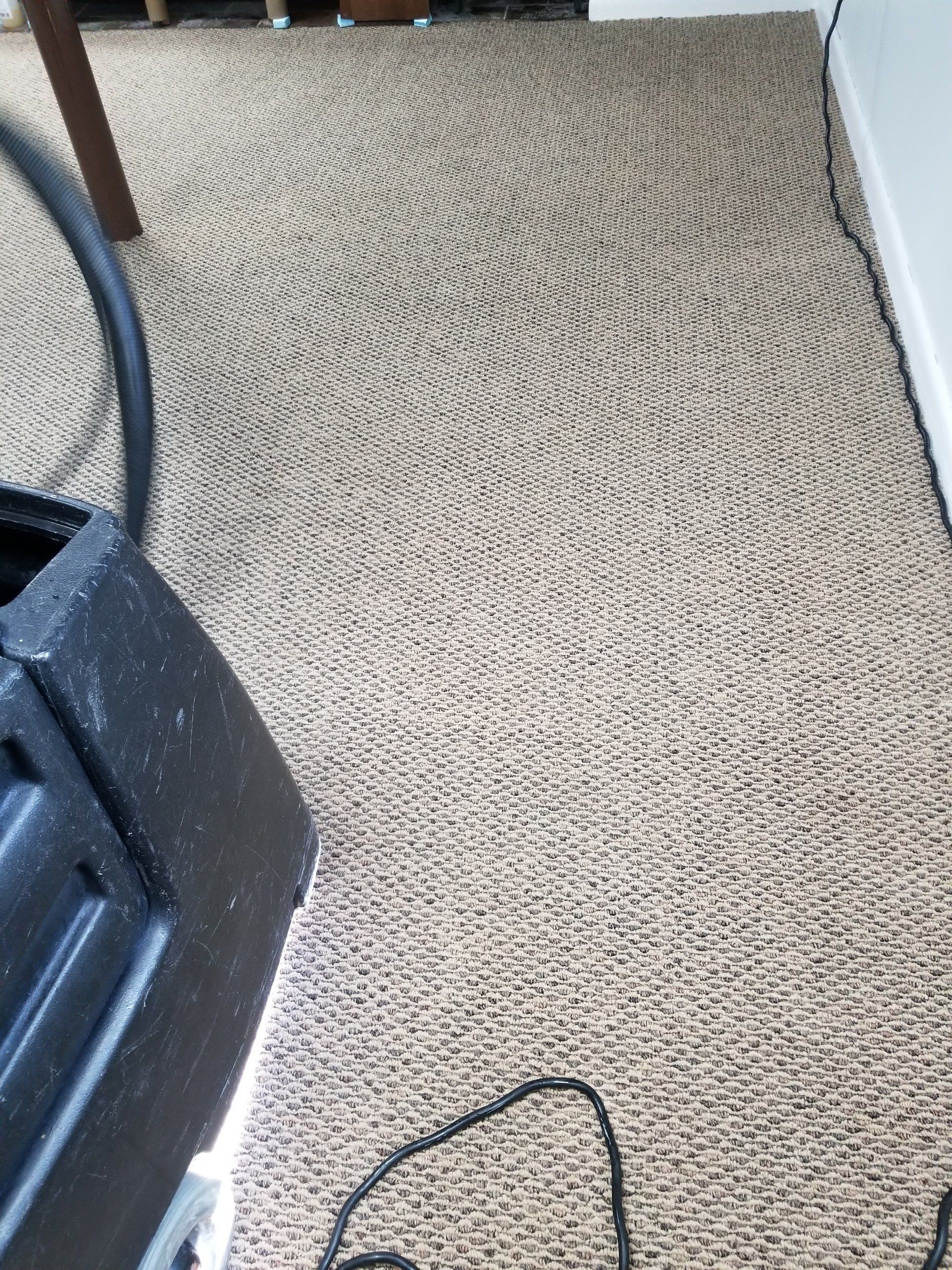 Vacuum marks in a zigzag pattern on brown, textured carpet next to a vacuum cleaner and a black cord.