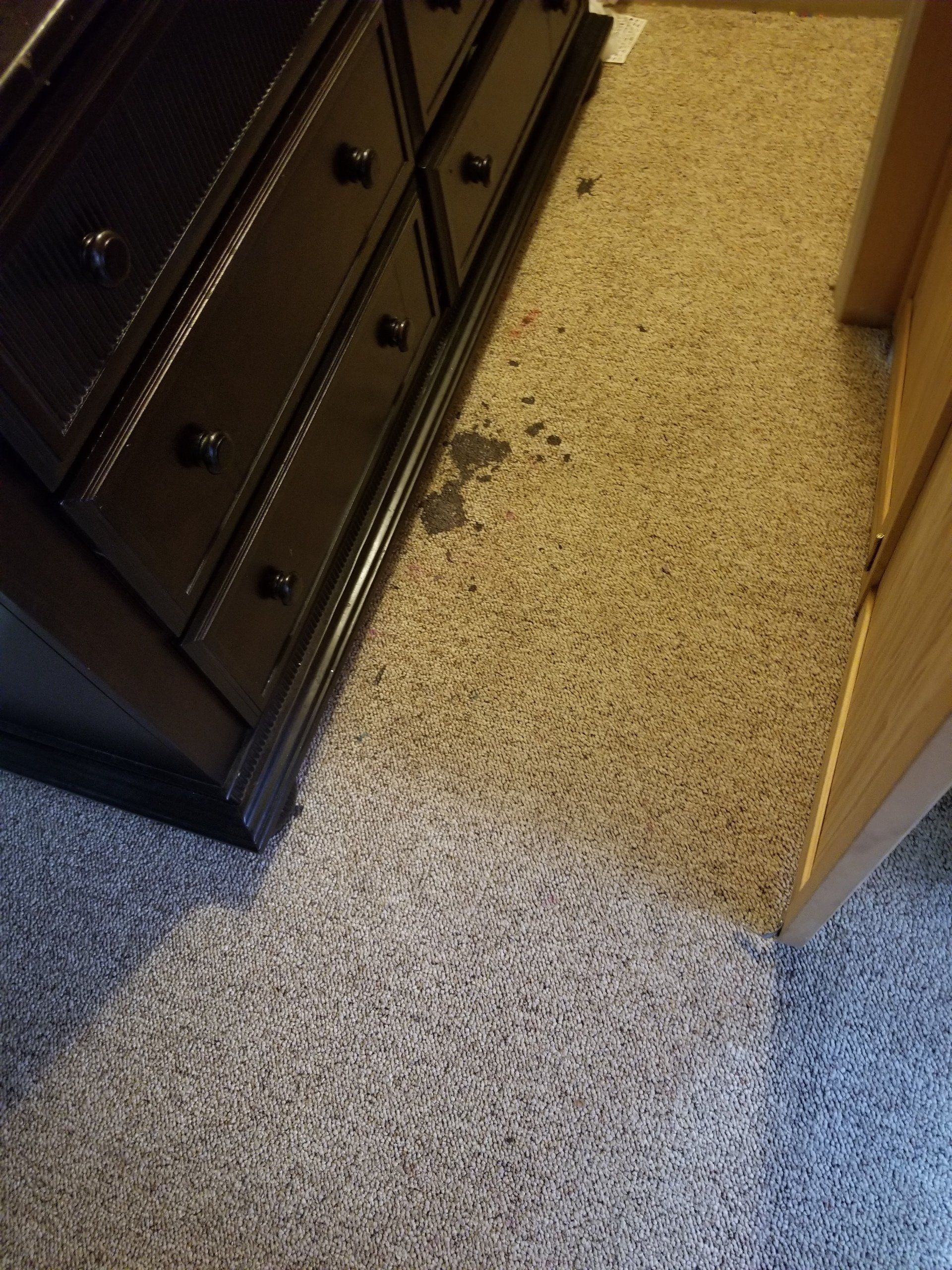 A dark wooden dresser sits on a carpeted floor next to a doorway, with visible dark spots or stains on the beige carpet.