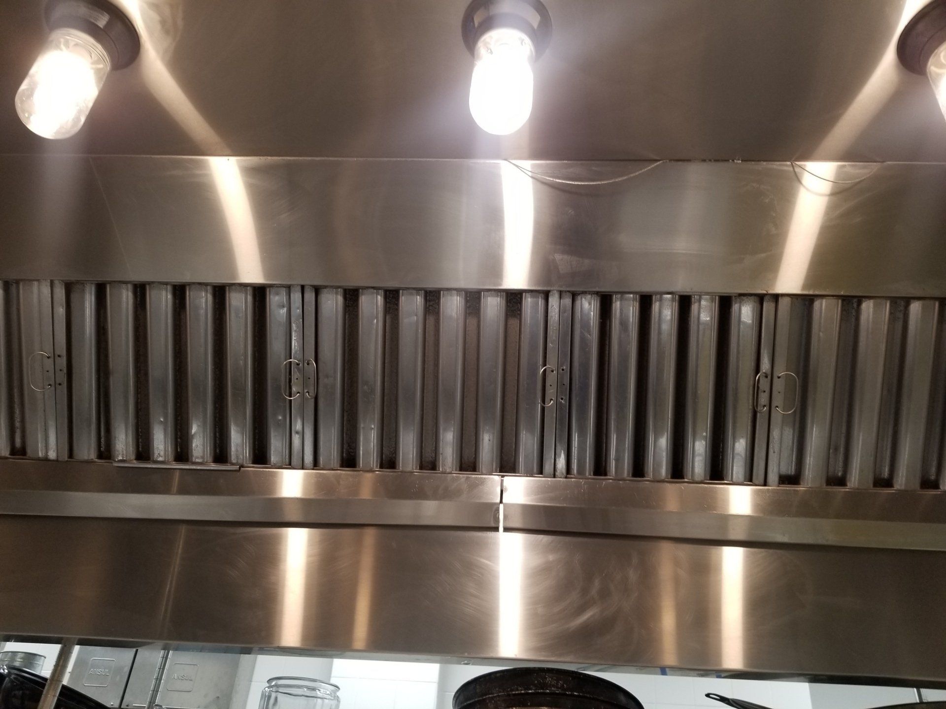 A stainless steel commercial range hood with baffle filters and three overhead light fixtures.