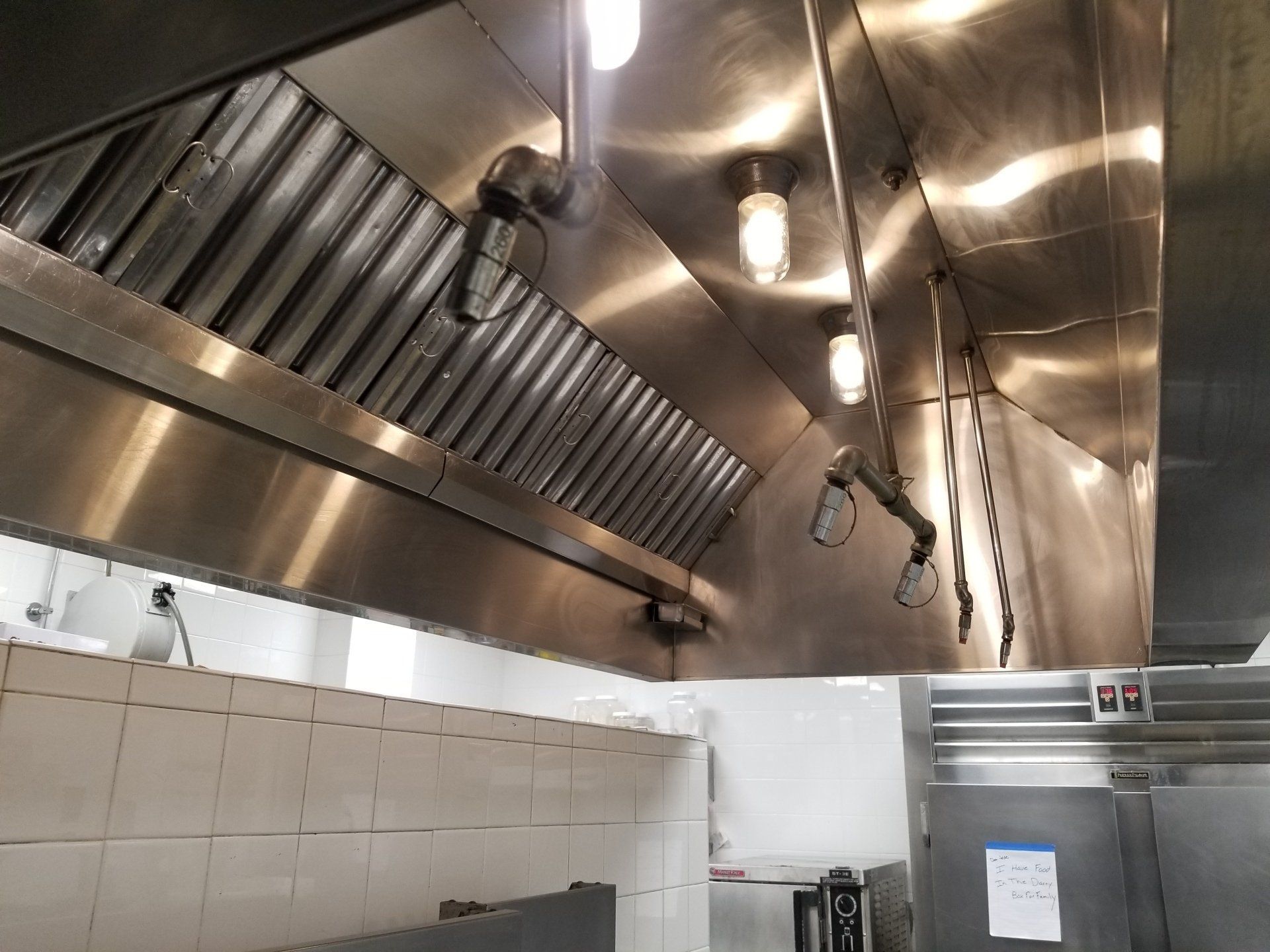 A stainless steel commercial kitchen hood with grease filters, integrated lights, and a fire suppression system nozzle.