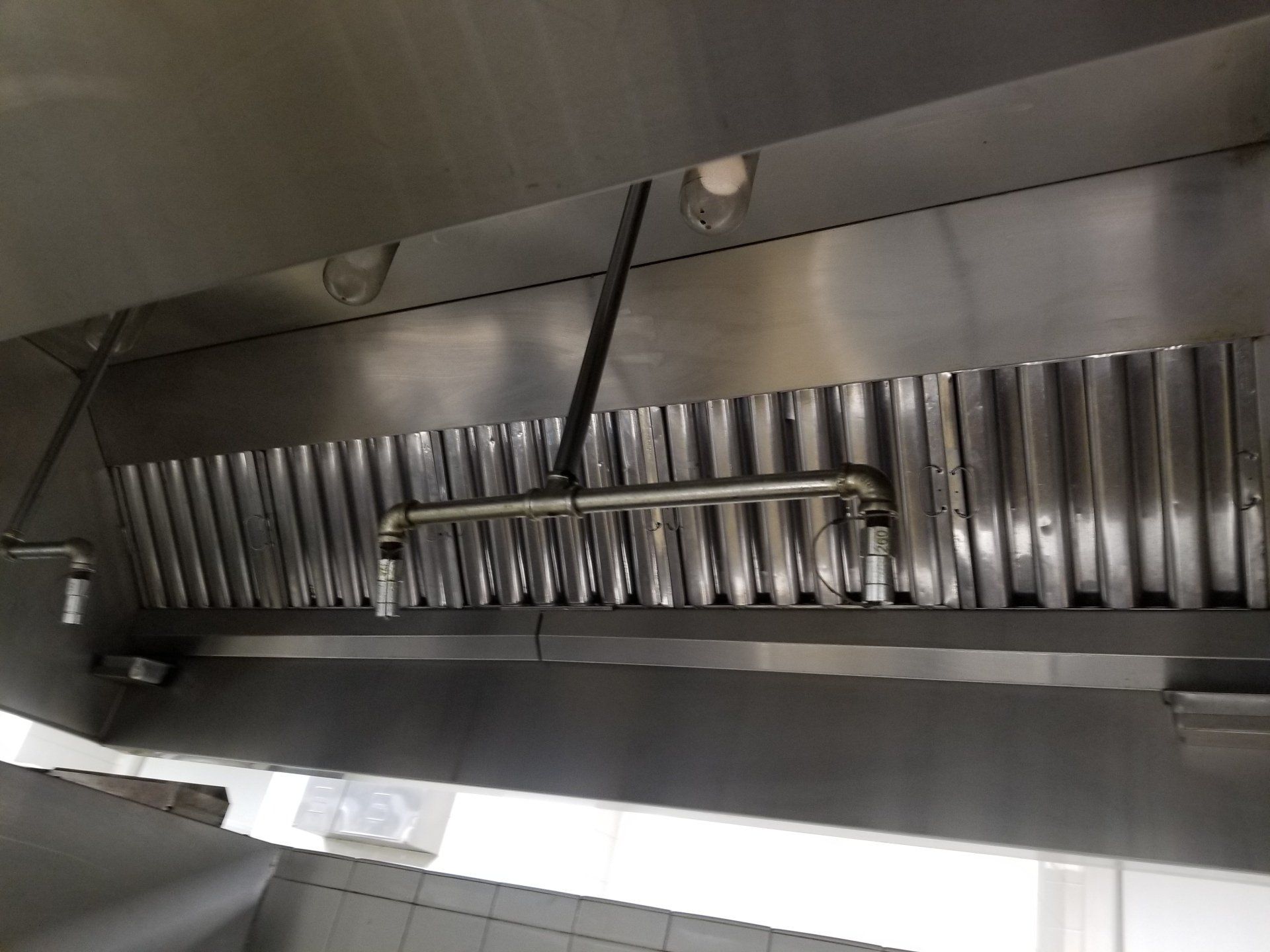 Industrial kitchen ventilation hood with stainless steel baffle filters and a fire suppression system nozzle.