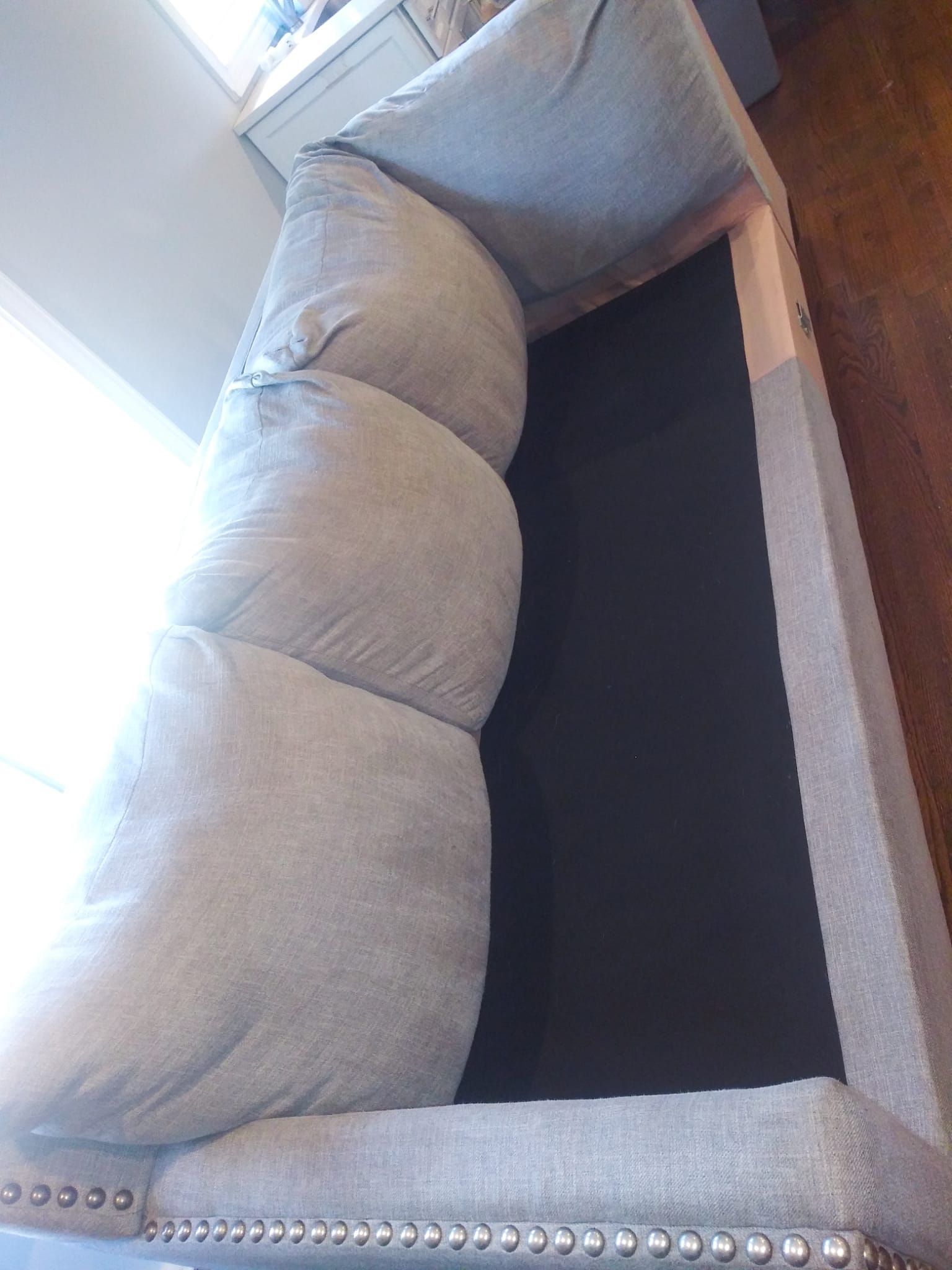 A gray sofa with tufted cushions on the back and decorative nailhead trim along the base, shown from an elevated angle.
