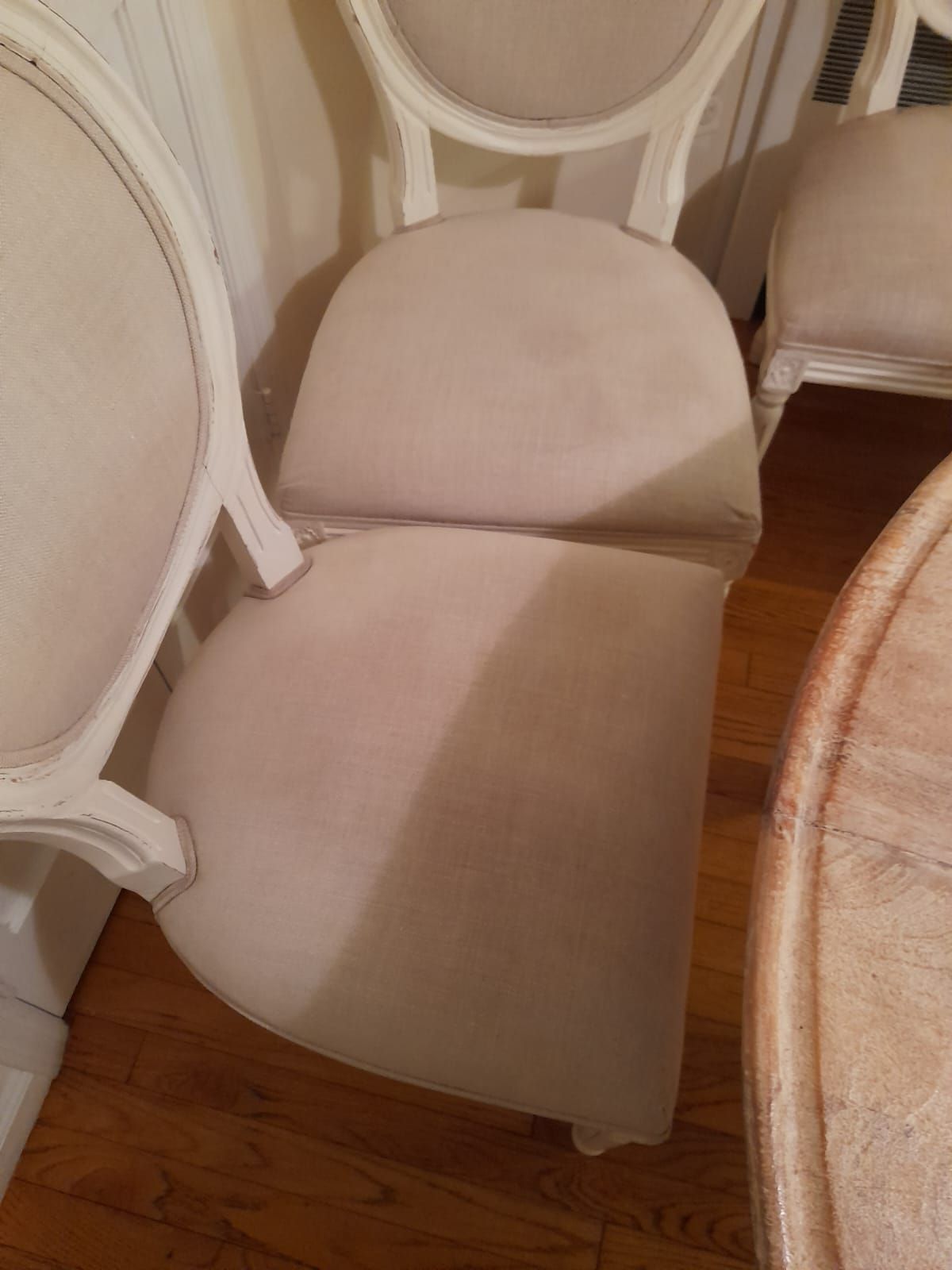 Close-up of several light beige upholstered dining chairs with white wooden frames arranged around a round table.