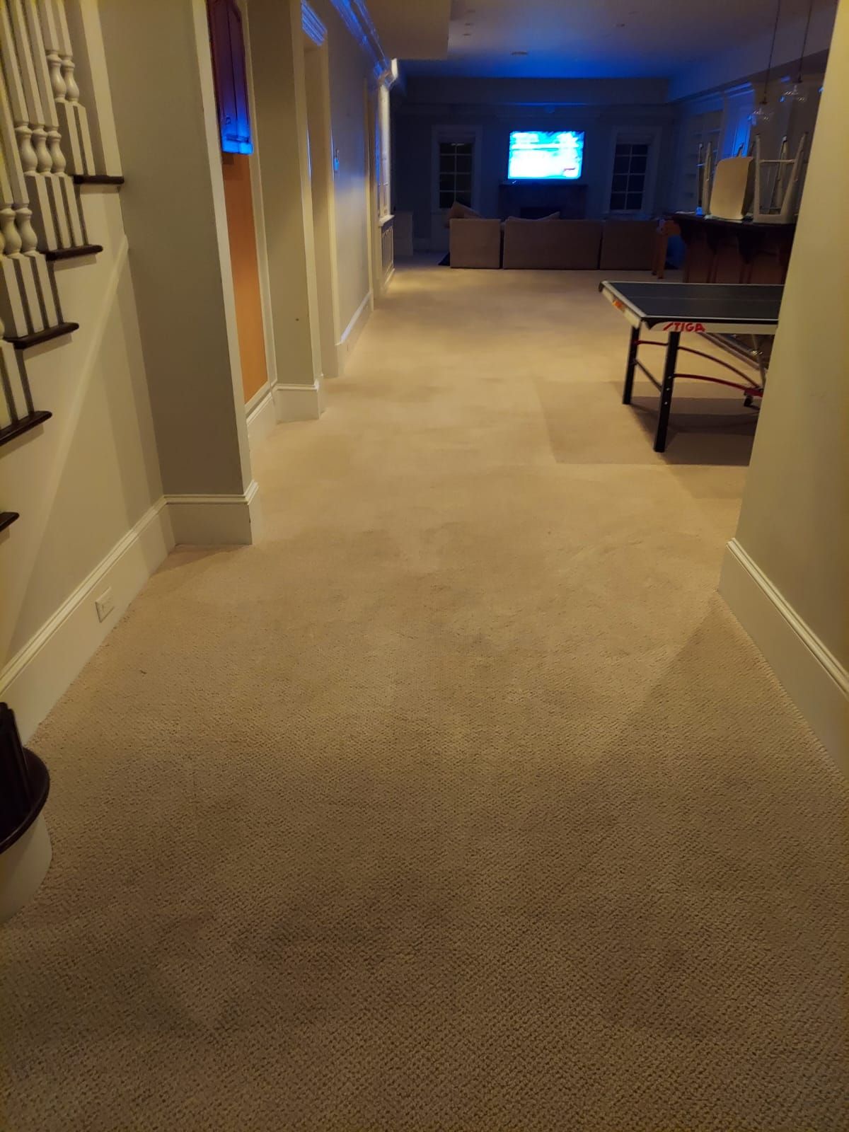 A carpeted hallway leads to a living area with a television, sofa, and a ping pong table.