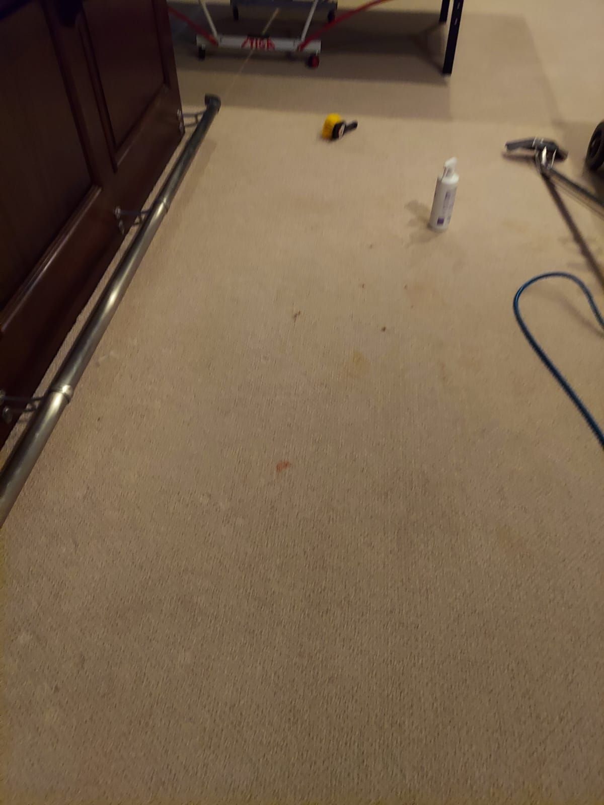 A high-angle view of beige carpet being cleaned, showing cleaning equipment, a bottle of solution, and scattered stains.
