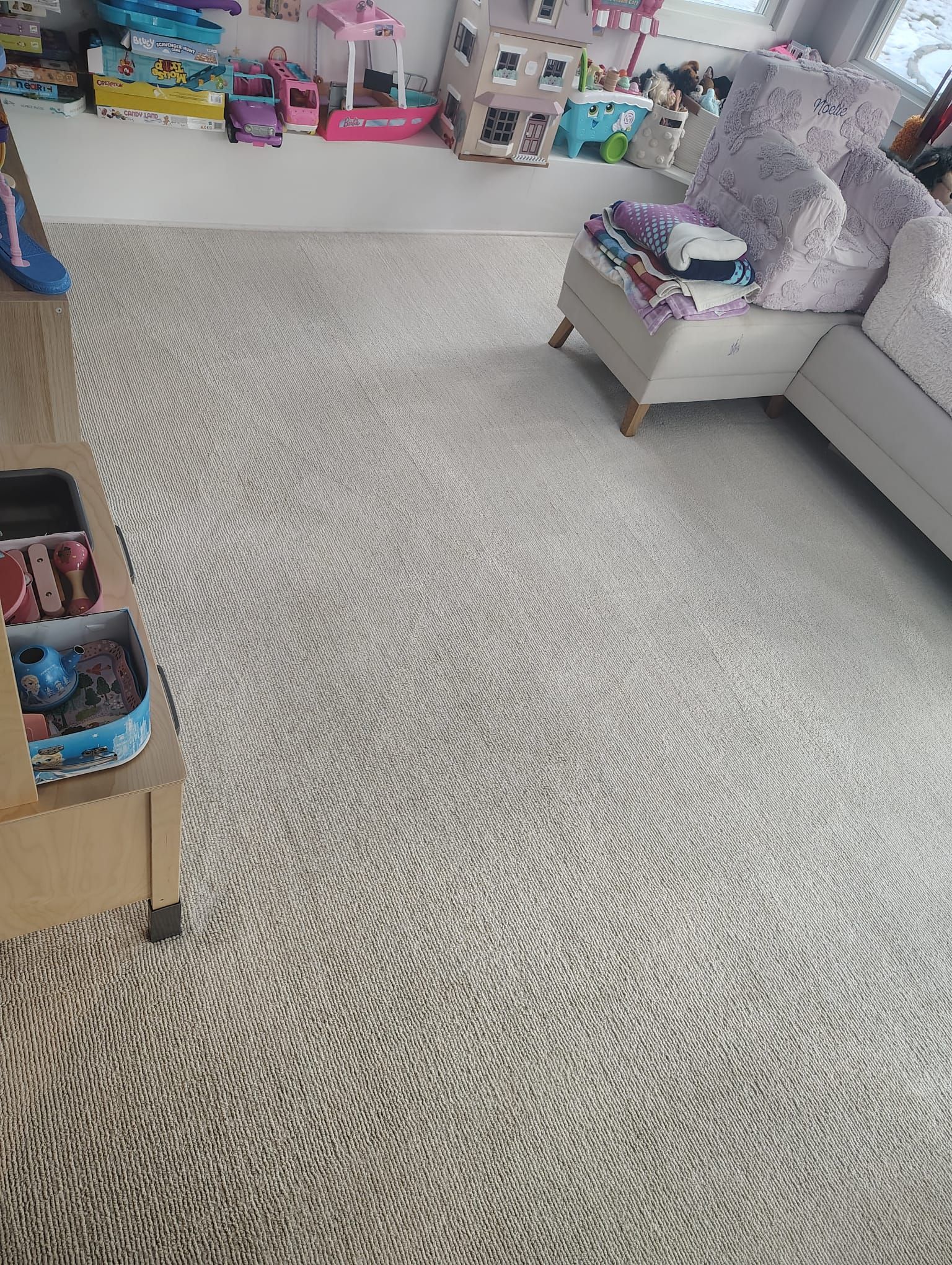 A high-angle view of a carpeted living room floor with a small storage unit, a plush chair, and toys on a shelf.