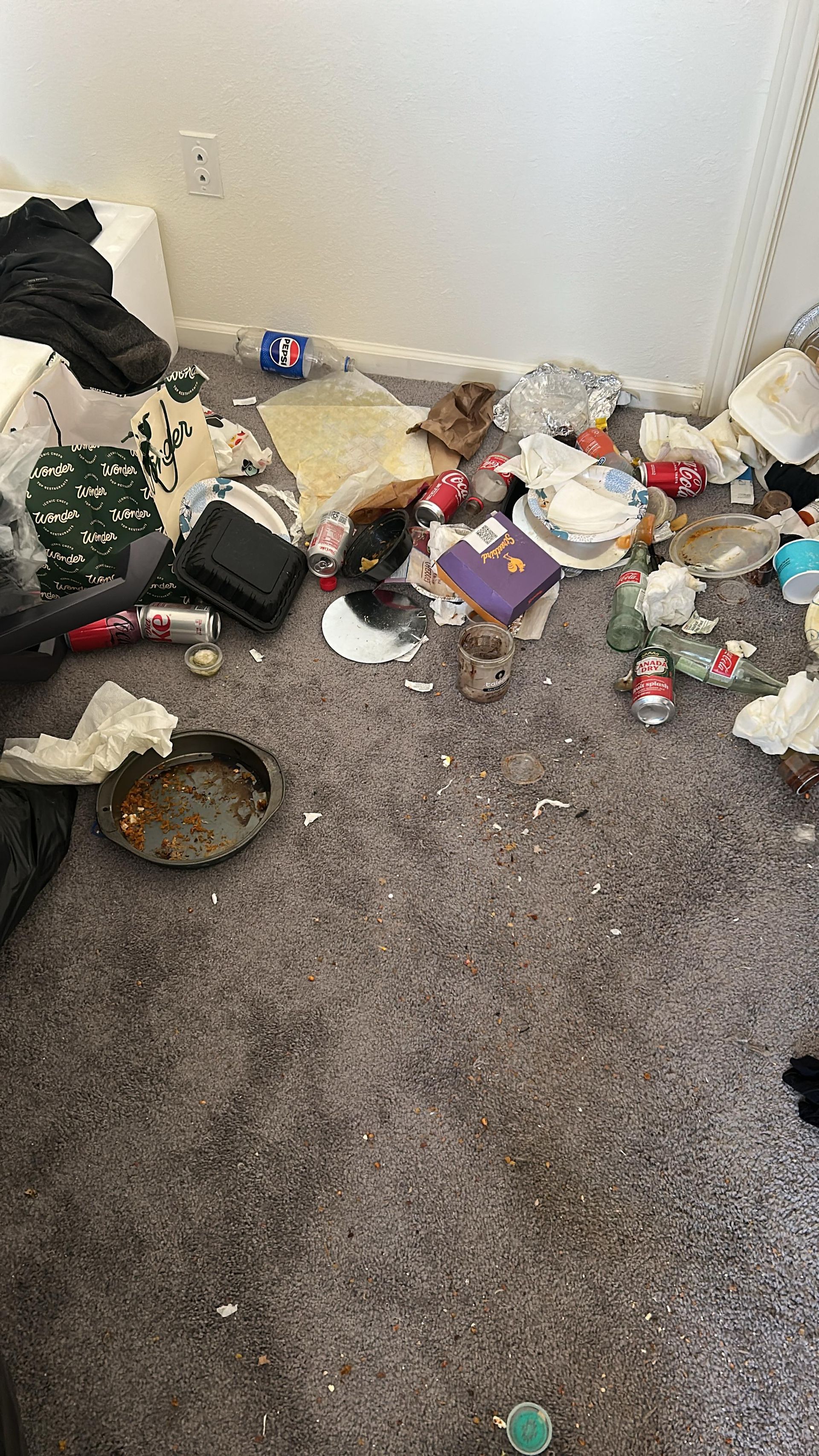 A messy room with scattered food containers, empty drink cans, debris, and discarded items covering the carpeted floor.