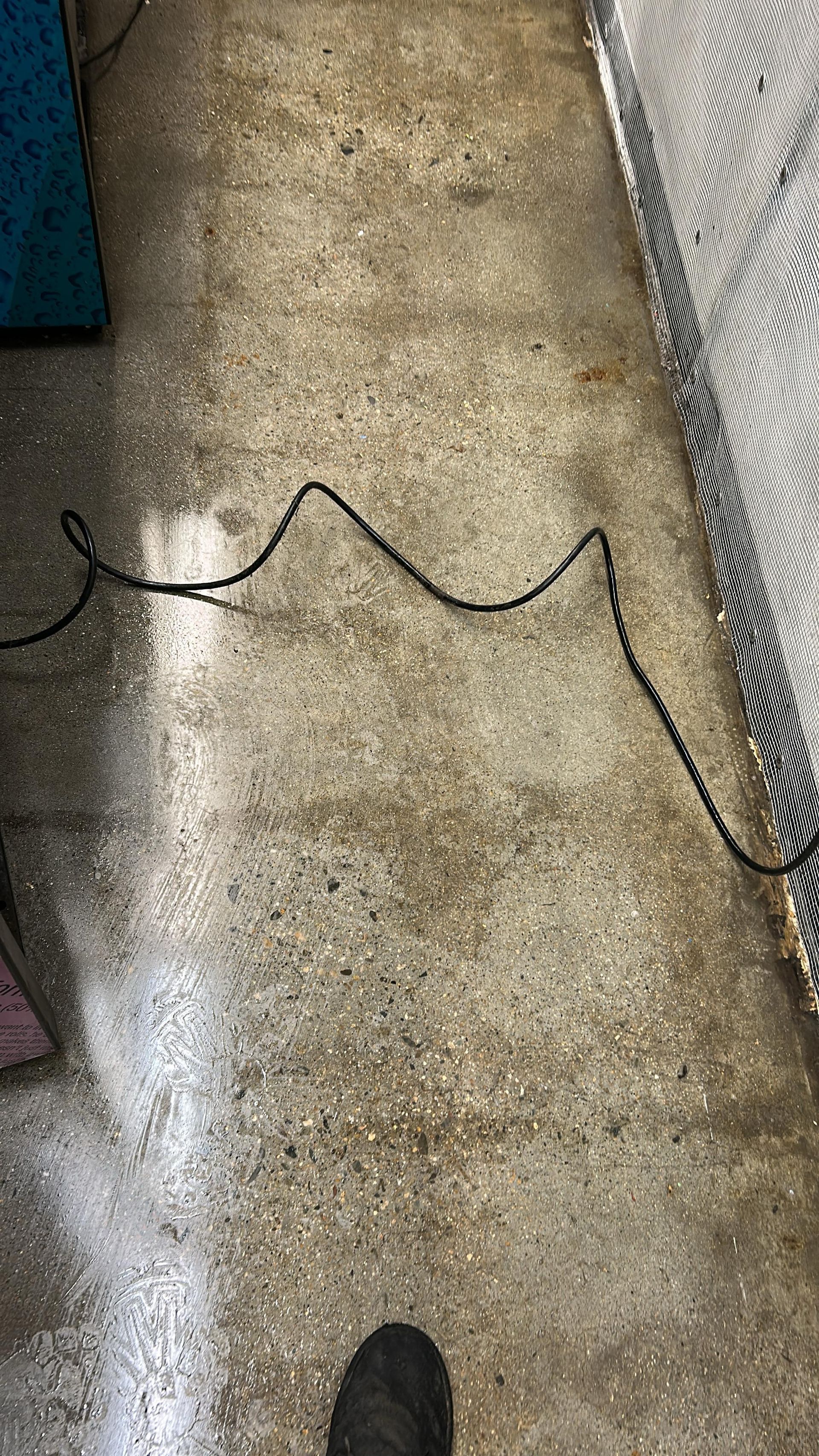 A black power cord stretches across a mottled gray concrete floor, with a dark shoe visible at the bottom edge.