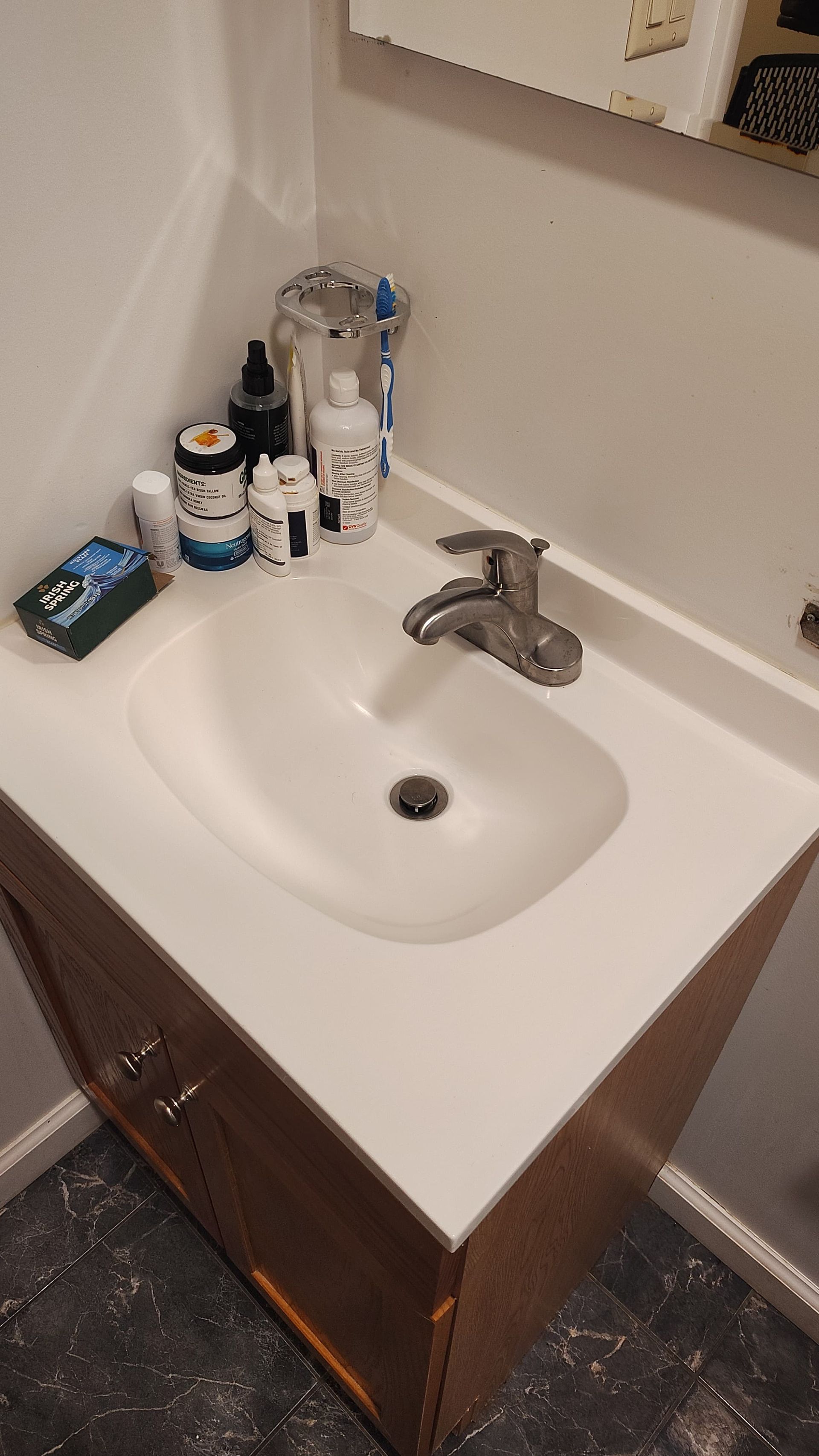 A bathroom vanity with a white sink and faucet, featuring various toiletries and a toothbrush arranged on the countertop.