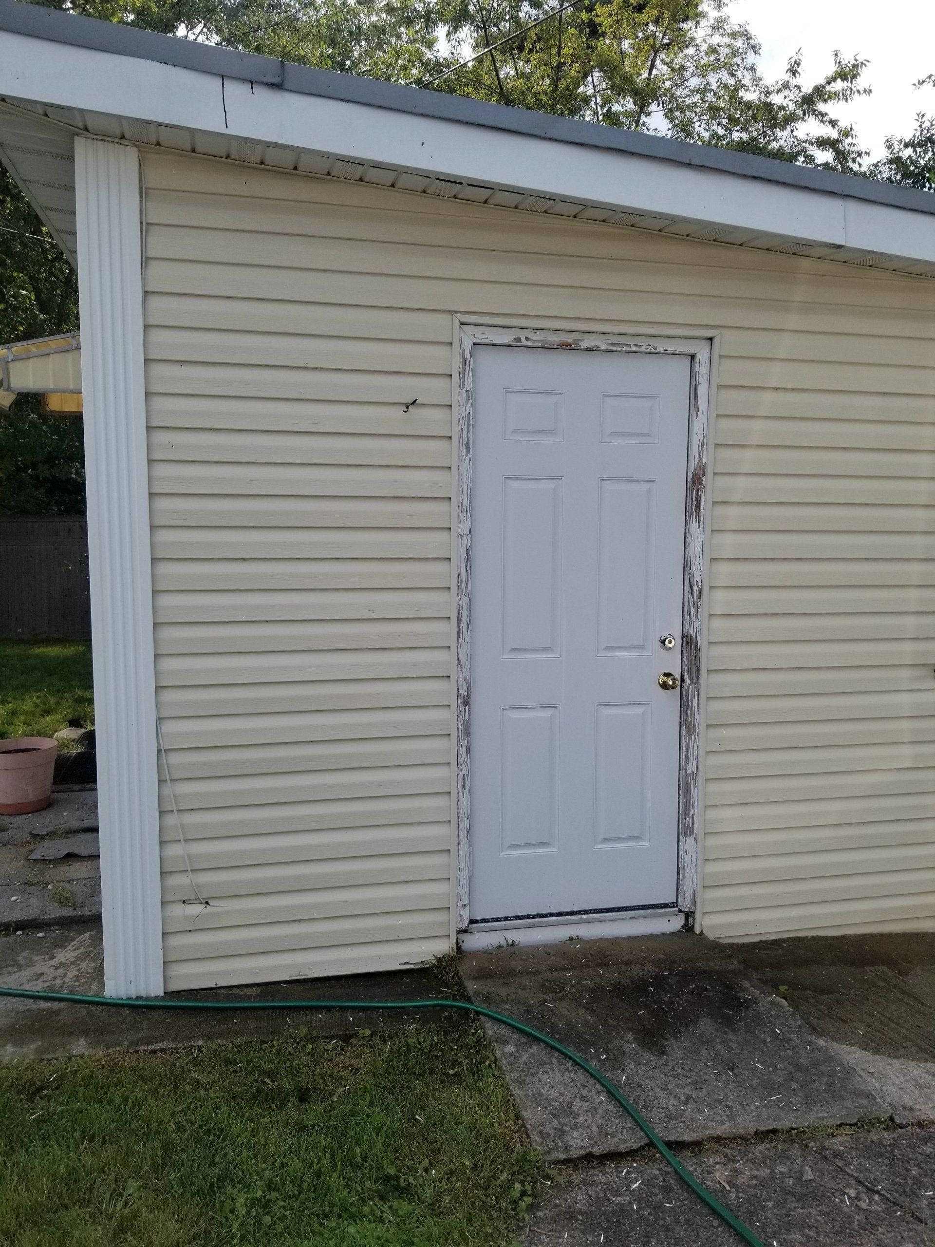 A white door set in a light yellow, horizontal-sided building exterior with chipped paint on the door frame.
