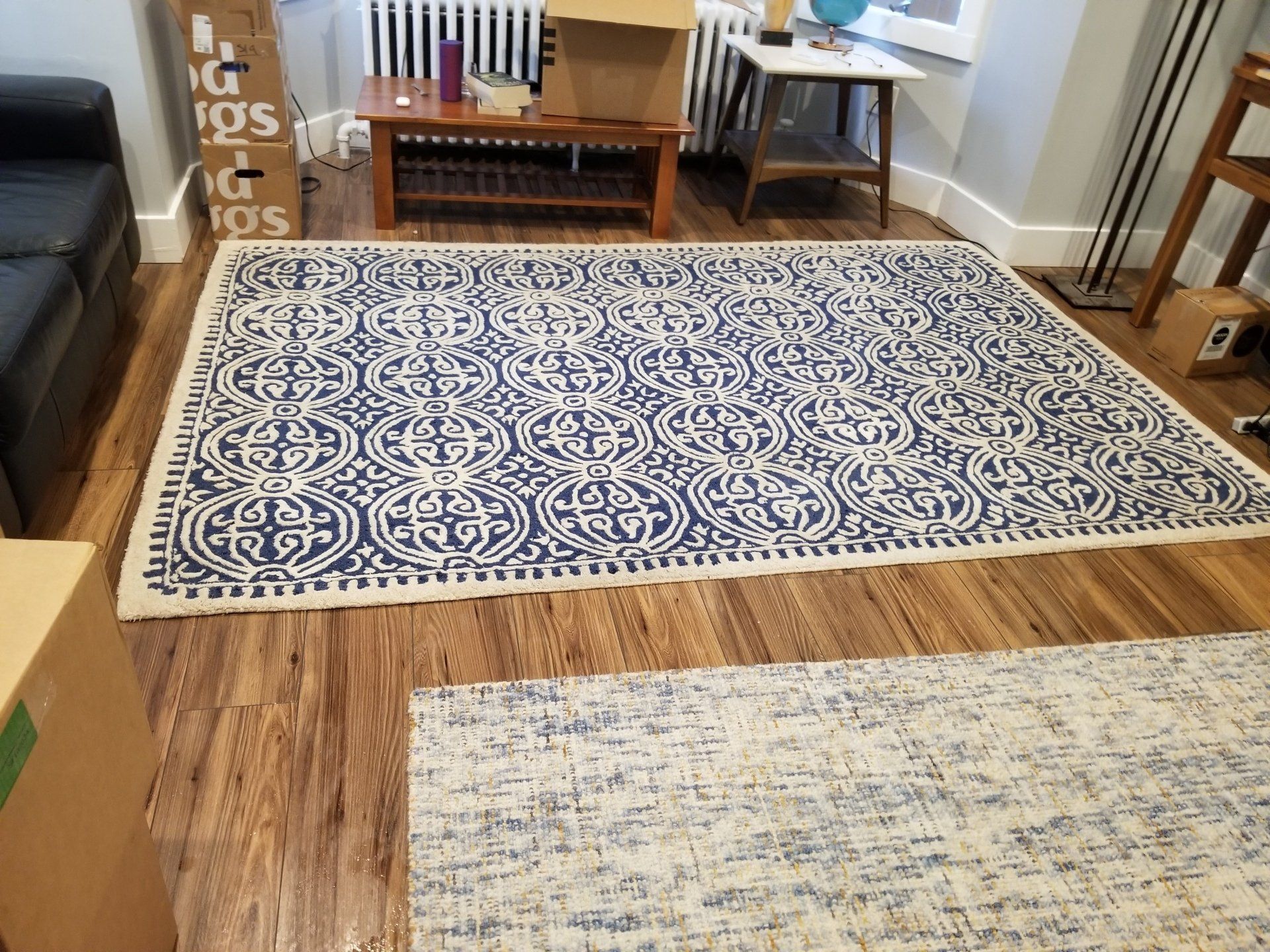 Two area rugs laid out on a wood floor in a living room, featuring a large blue-and-white patterned rug and a textured rug.