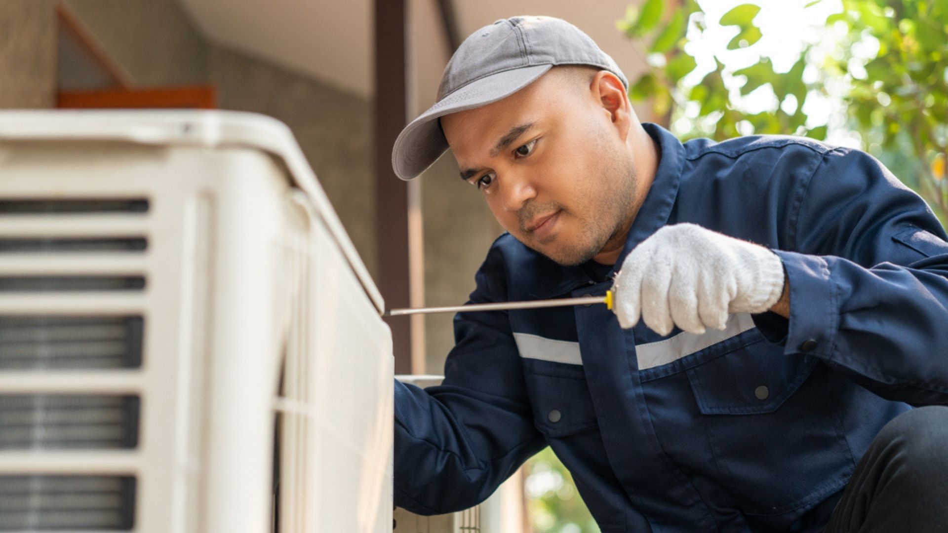 Technician inspecting an outdoor air conditioner unit with a screwdriver