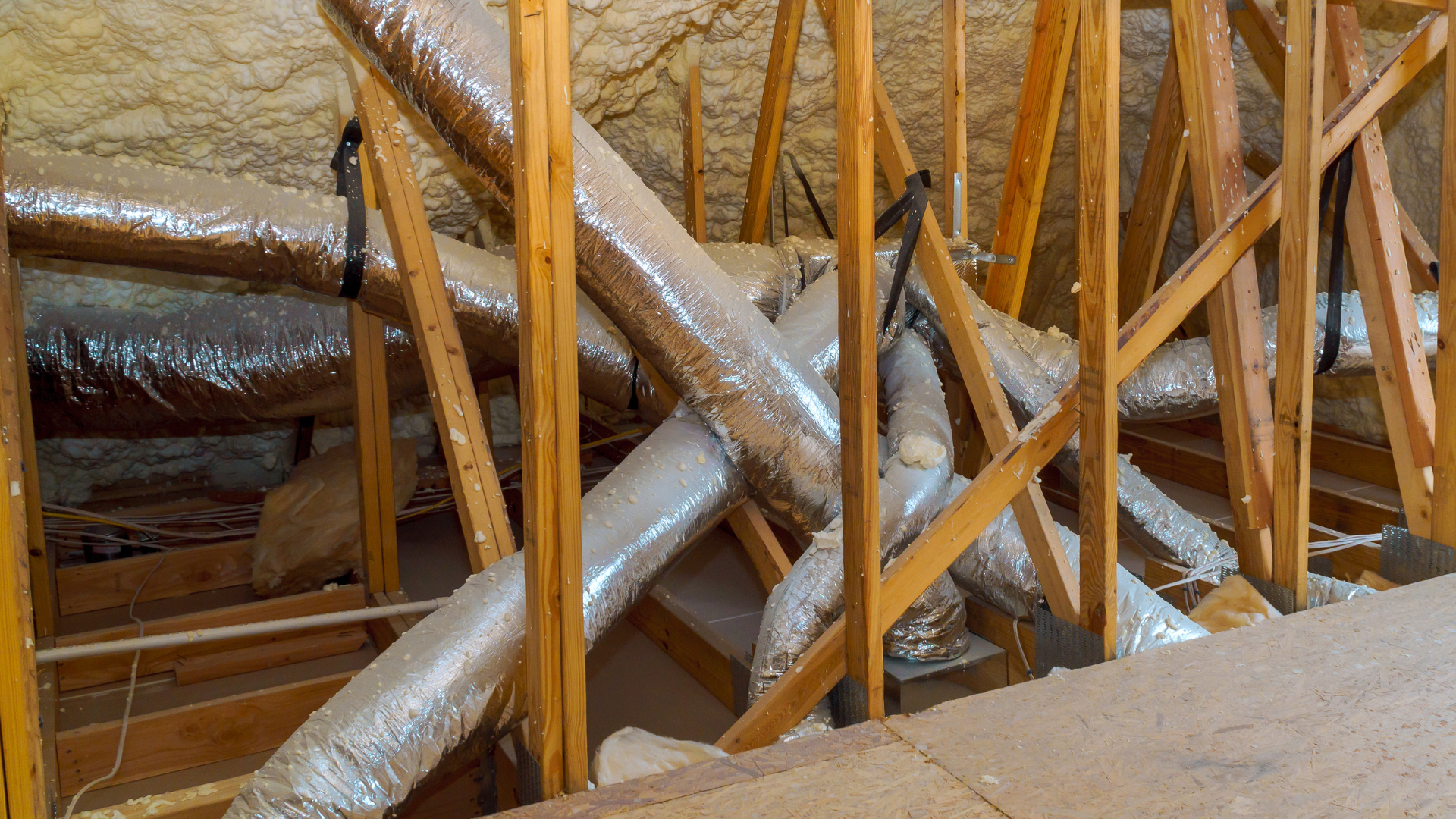 Silver insulated ducts and wooden framing inside an attic or crawlspace