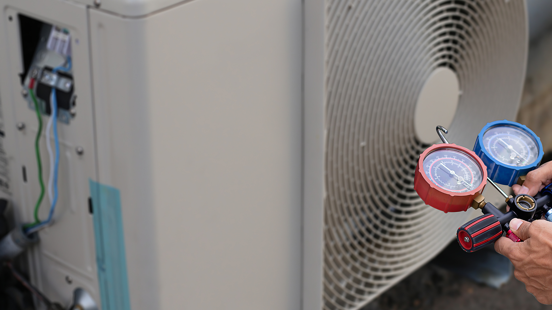 Technician holding gauges near an outdoor HVAC unit, checking refrigerant pressure.