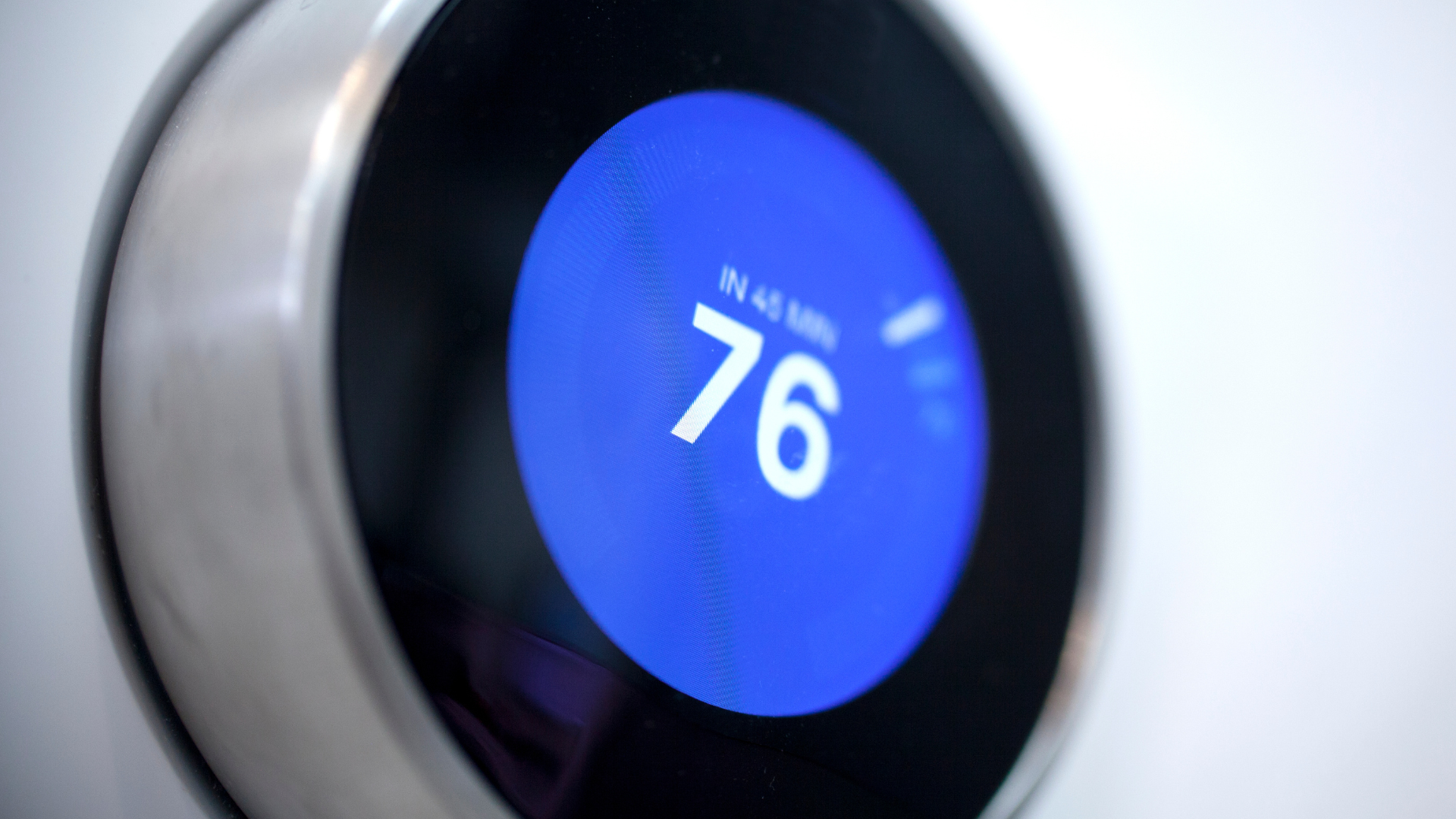 Close-up of a round smart thermostat showing 76 on a blue display.
