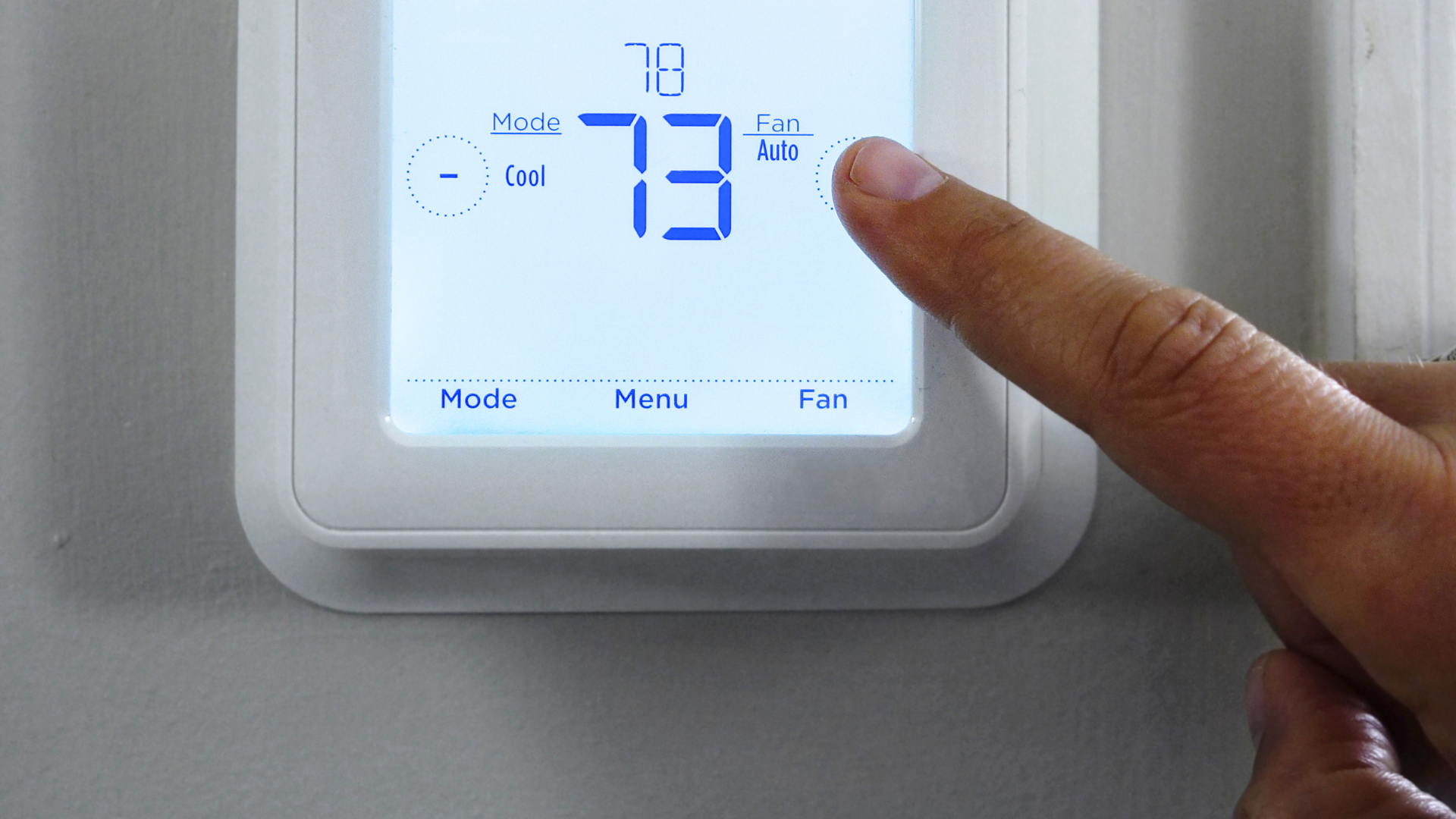 Finger touching a white touchscreen smart thermostat displaying 73°F with blue backlit controls.