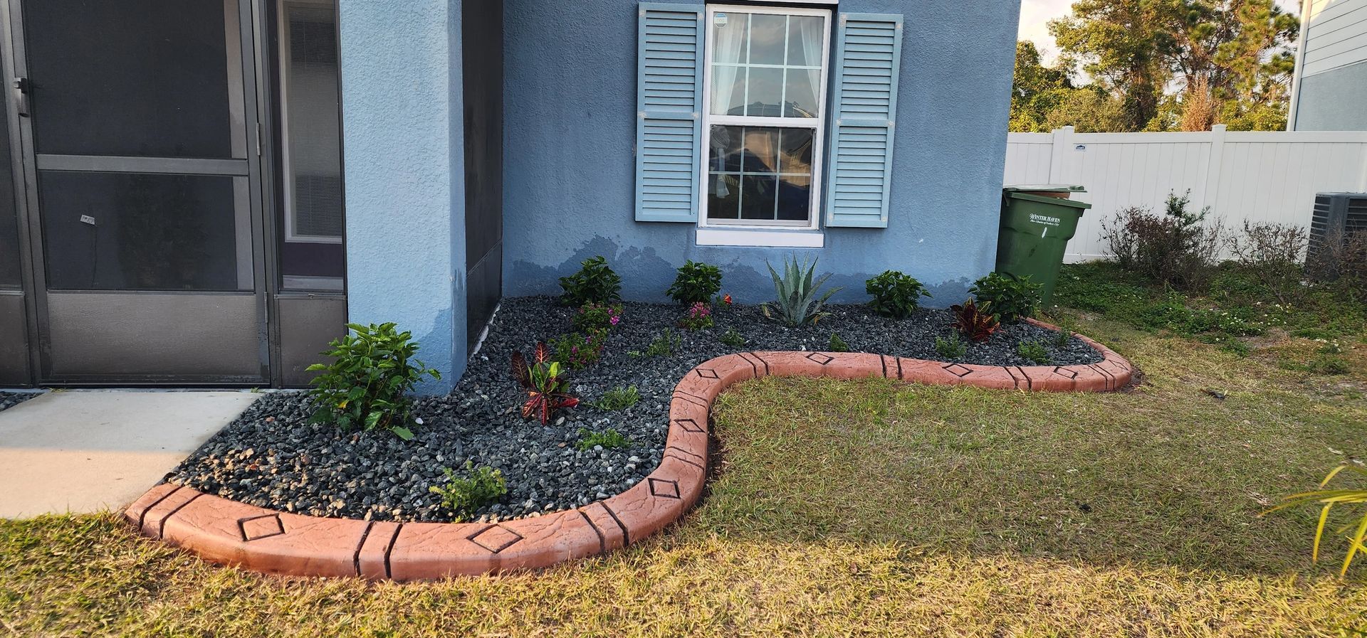 A house with blue walls and a small garden bed edged with red brick.