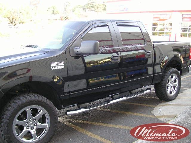 Black lifted pickup truck parked in a lot, side view, with chrome step bars and silver wheels