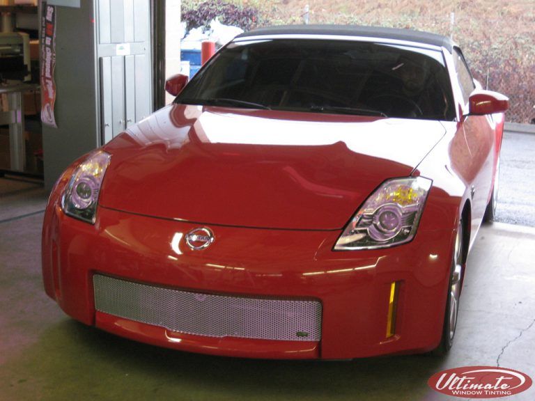 Red sports car in a garage, front view with a silver mesh grille and tinted windshield
