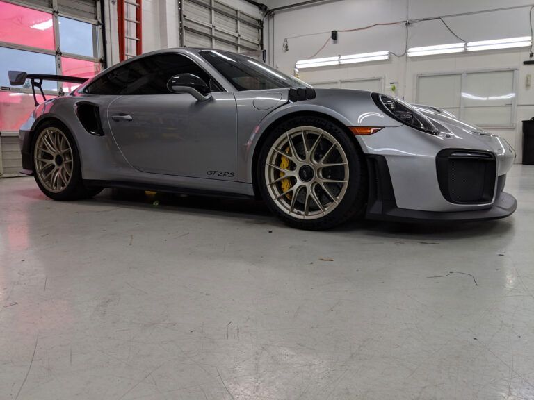 Silver sports car in a garage, low angle view, with bronze wheels and yellow brake calipers.