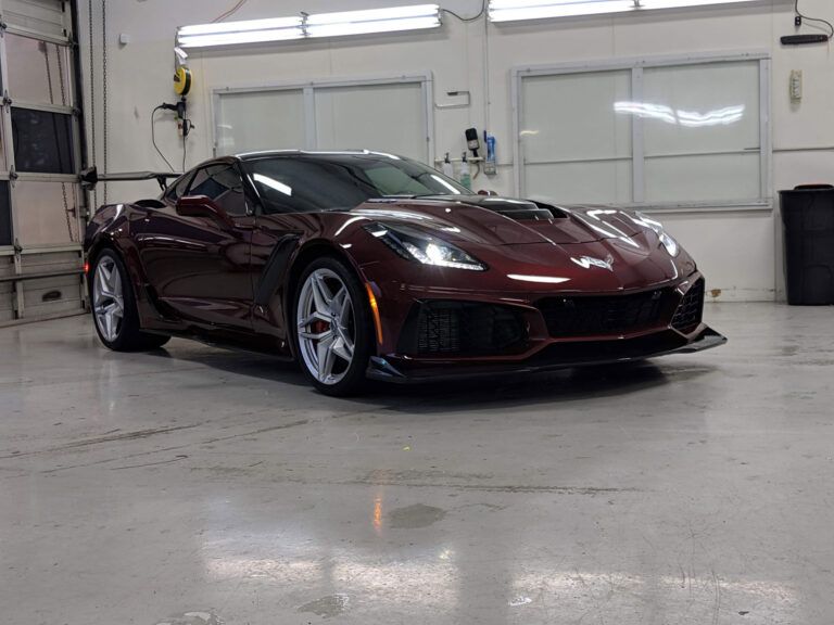 Maroon sports car parked in a bright garage with white walls and concrete floor