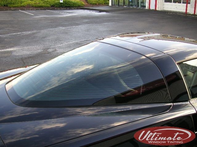 Close-up of a black car roof and rear window with red and white building in the background