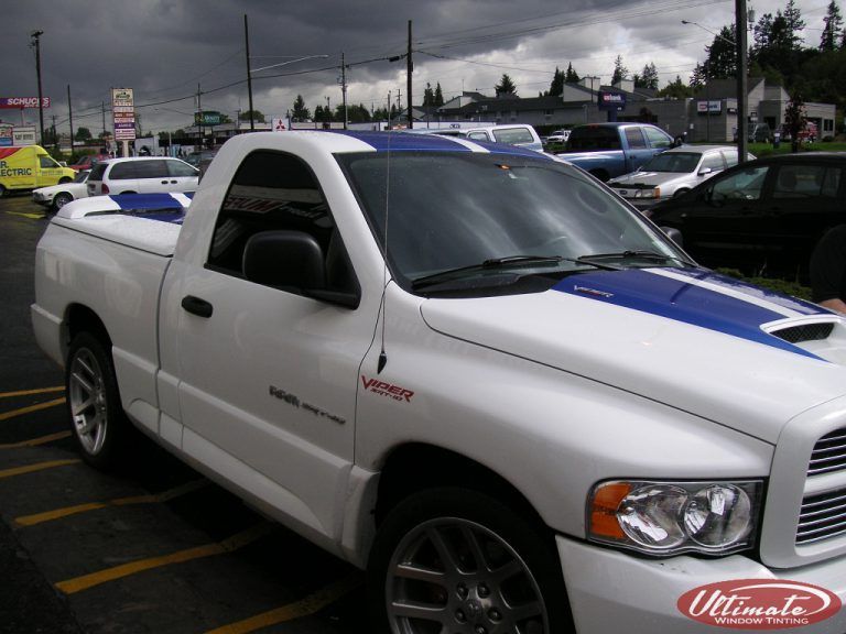 White Toyota pickup truck with blue racing stripes parked at an outdoor lot under cloudy skies