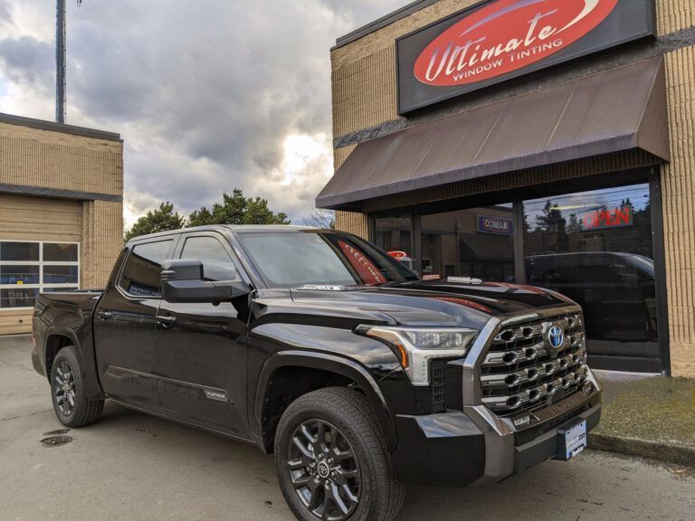 Black pickup truck parked outside a storefront with a red awning.