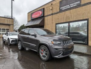 Two SUVs parked outside a wet car dealership on a rainy day