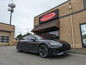 Black sports coupe parked outside a brick building with an awning and red sign.