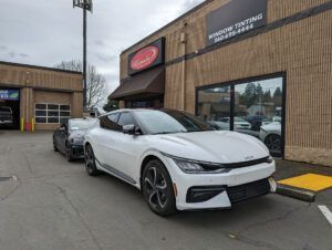 White sports sedan parked outside a storefront on a city street, with a second car behind it.