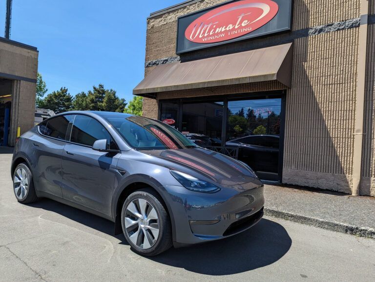 Gray Tesla parked outside a storefront with a red awning and sign.