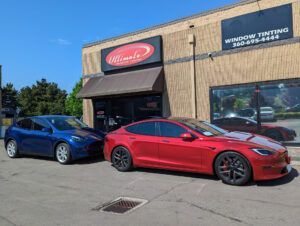 Blue and red cars parked outside a window tinting shop on a sunny day