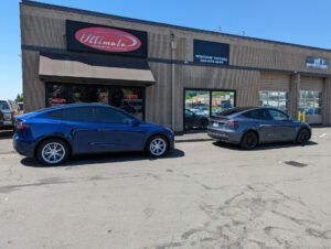 Two parked cars outside a storefront on a sunny street.