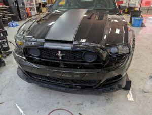 Black Ford Mustang with silver racing stripe in an auto shop garage