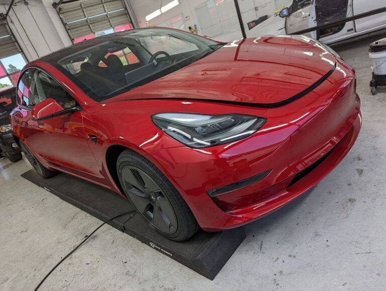 Red Tesla sedan in a garage, angled front-left view with black wheels and a red exterior