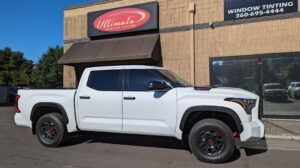 White pickup truck parked outside a window tinting shop on a sunny day