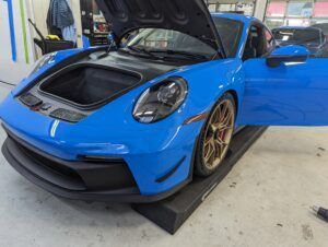 Blue sports car with hood open in a garage, shown on a lift with gold wheels.