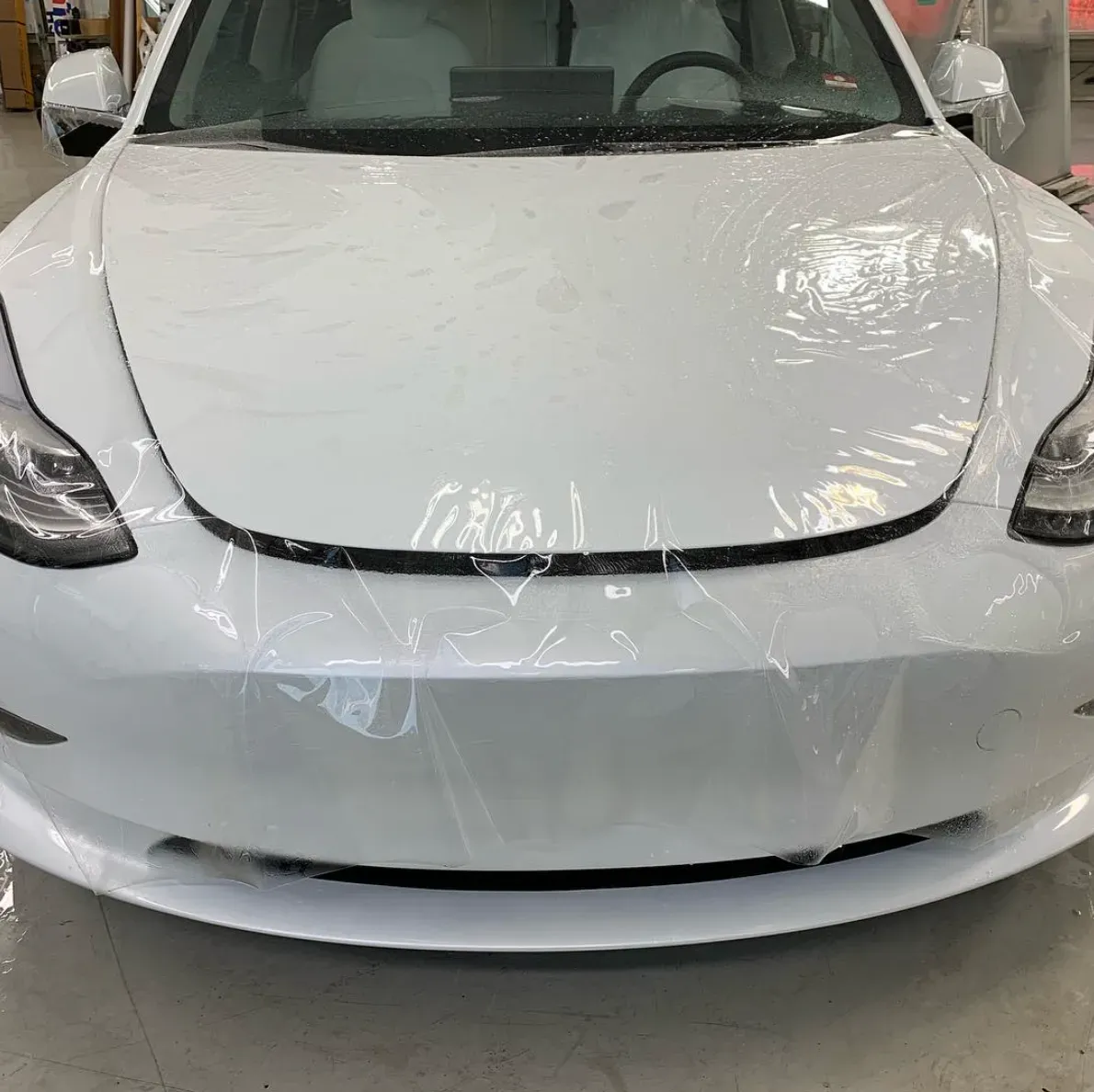 White car front view covered in protective plastic wrap indoors