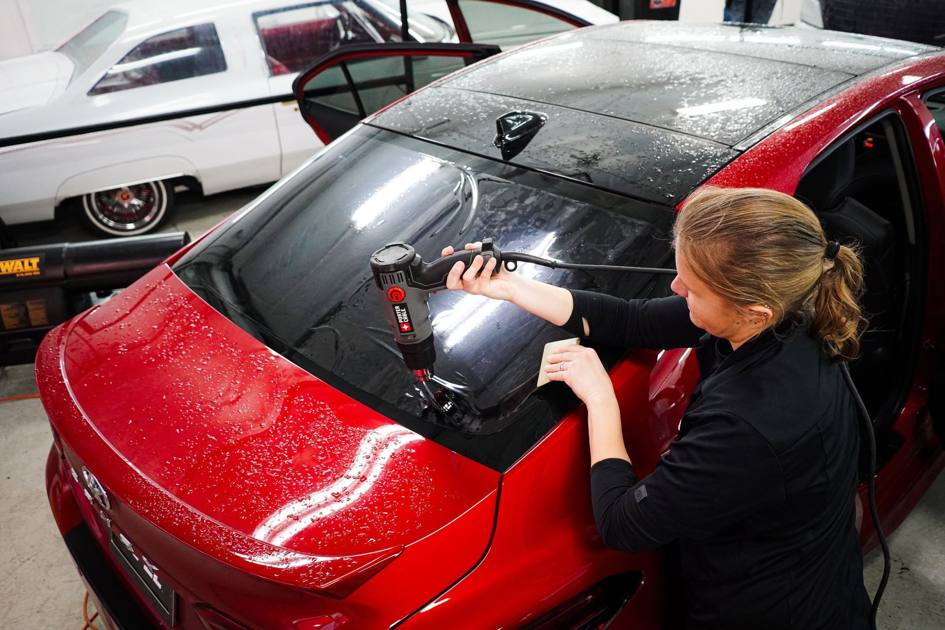 Ultimate Window Tinting technician installing ceramic window film on a red sedan's rear windshield in Portland