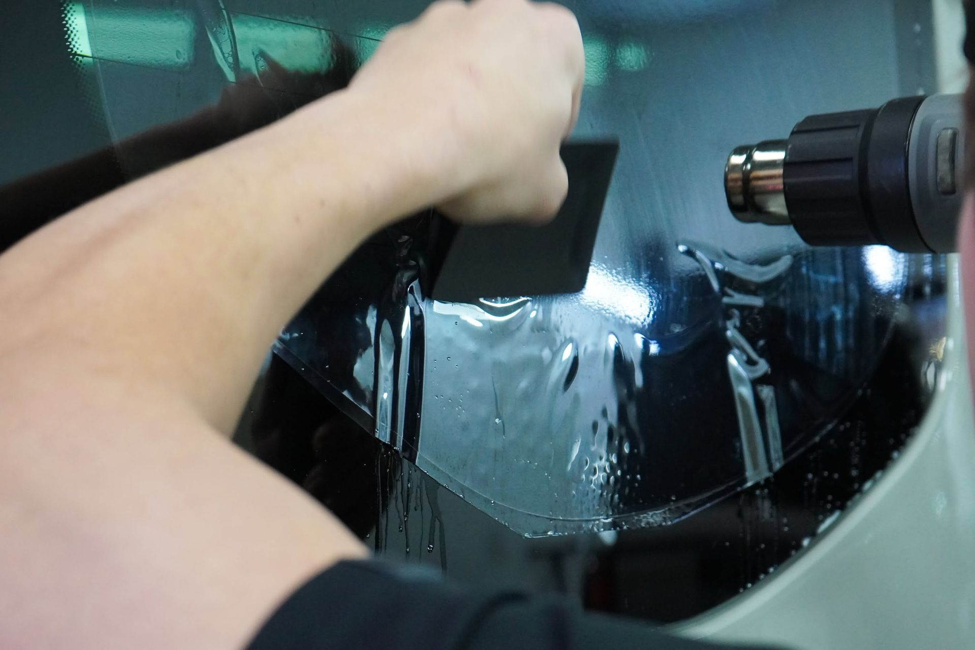 Person using a drill on a wet car windshield during repair