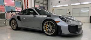 Silver Porsche sports car parked indoors in a garage, front three-quarter view with yellow brake calipers