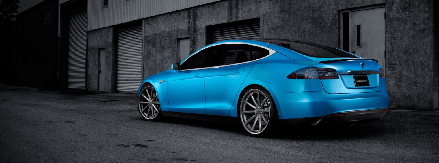Blue sports sedan parked in front of an industrial garage wall