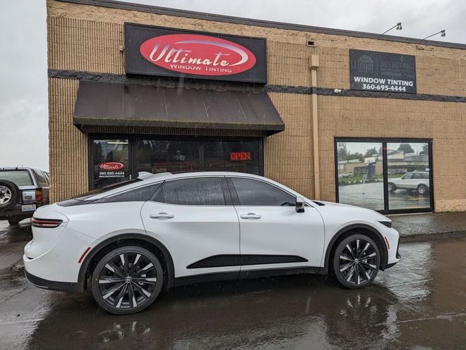 White SUV parked outside a storefront with a red sign on a wet street.