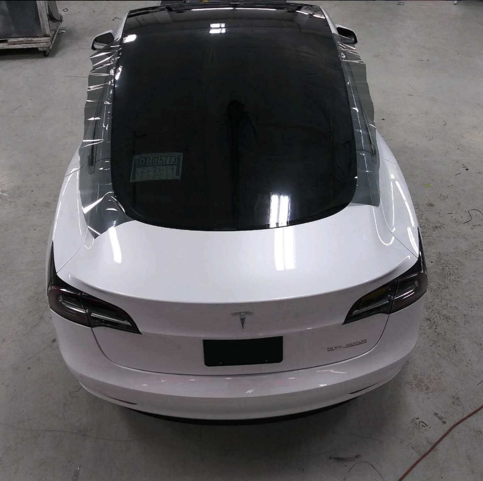 White Tesla sedan viewed from above in a garage, with a black roof and rear window.