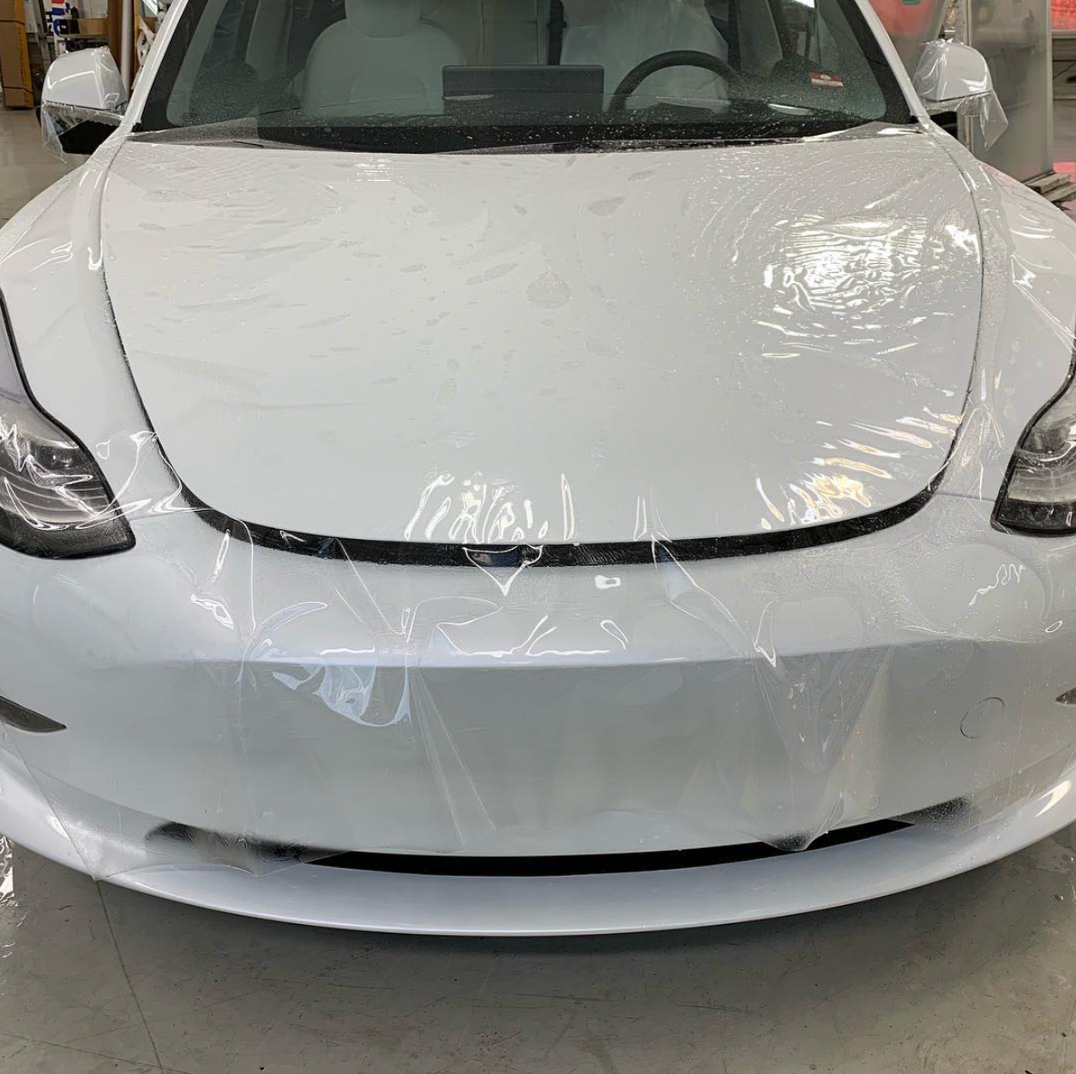 Front view of a white car wrapped in protective plastic film indoors