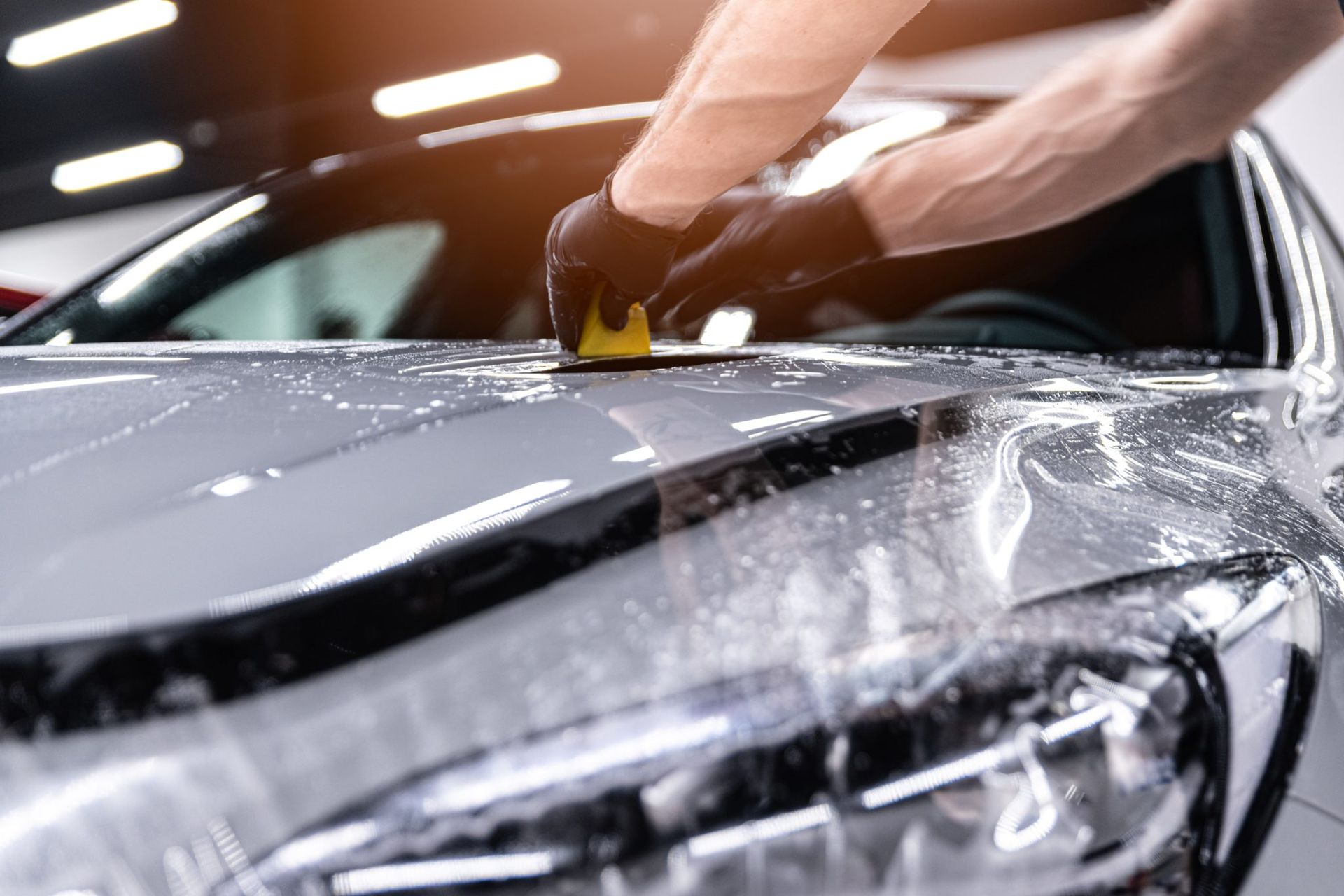 Hand applying protective film to a car hood and headlight in a workshop